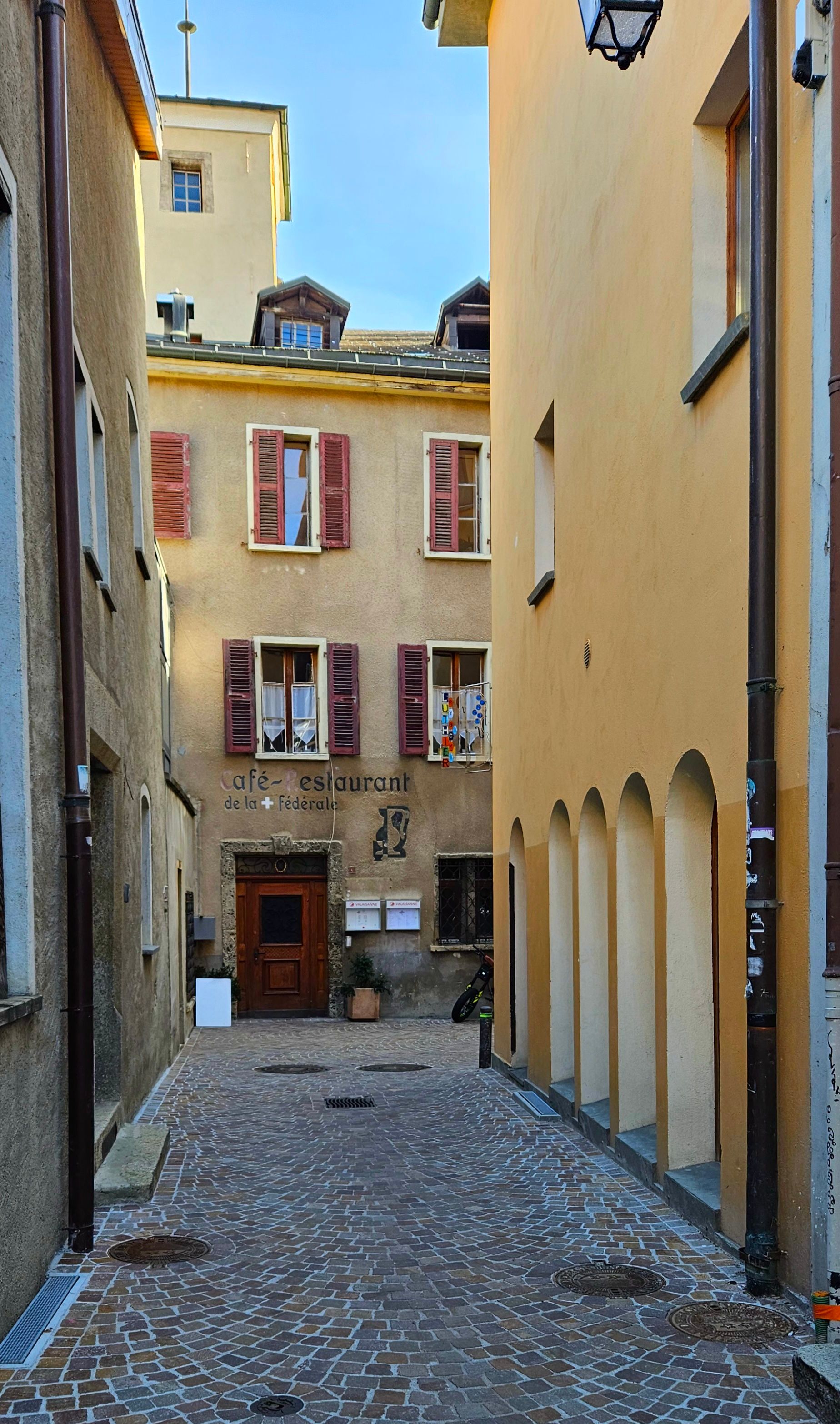 Narrow European alleyway featuring rustic buildings and vintage architecture under a clear sky.