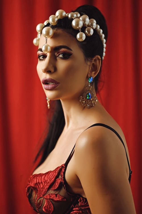 Free Stylish portrait of a woman wearing a red dress and a pearl-adorned headpiece against a red backdrop. Stock Photo