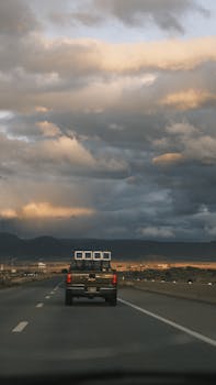 A truck driving on a highway with dramatic clouds and mountains in the background.