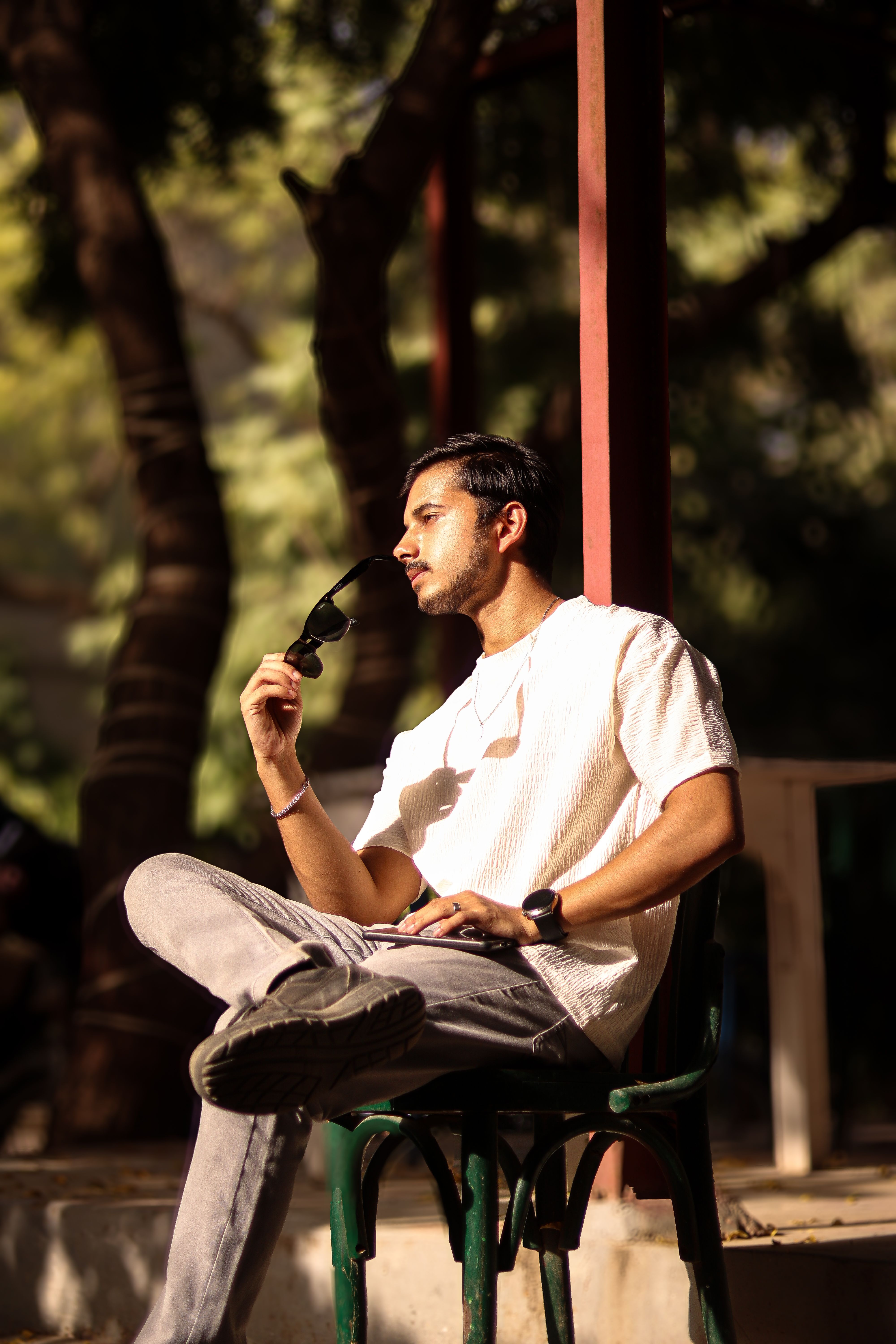 A young man sits outdoors, relaxing with sunglasses, enjoying sunny weather.