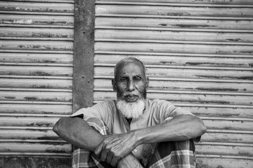 Free Black and white portrait of an elderly man seated against a shutter in Dhaka, Bangladesh. Stock Photo