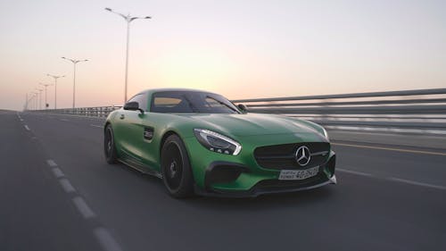 Modern green luxurious vehicle with glossy surface driving along barrier at sunset