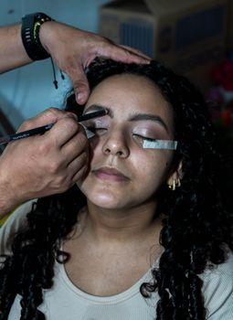 Makeup artist applying eyeshadow with precision on woman's face indoors.