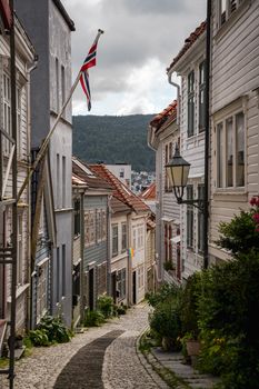 Charming cobblestone street in Bergen, Norway, lined with colorful wooden houses and flags.
