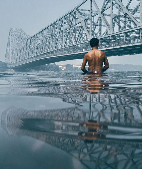 Free Man wading in water by Howrah Bridge in Kolkata, India. Reflective and serene scene. Stock Photo