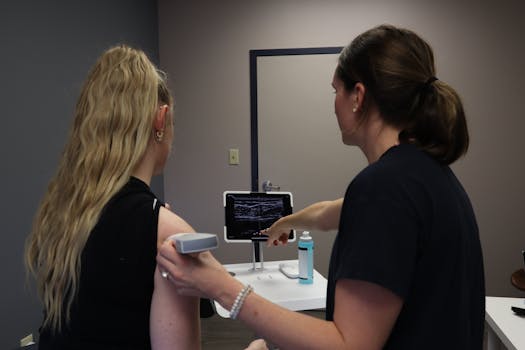 A healthcare professional performs an ultrasound shoulder scan, pointing at the screen for analysis.