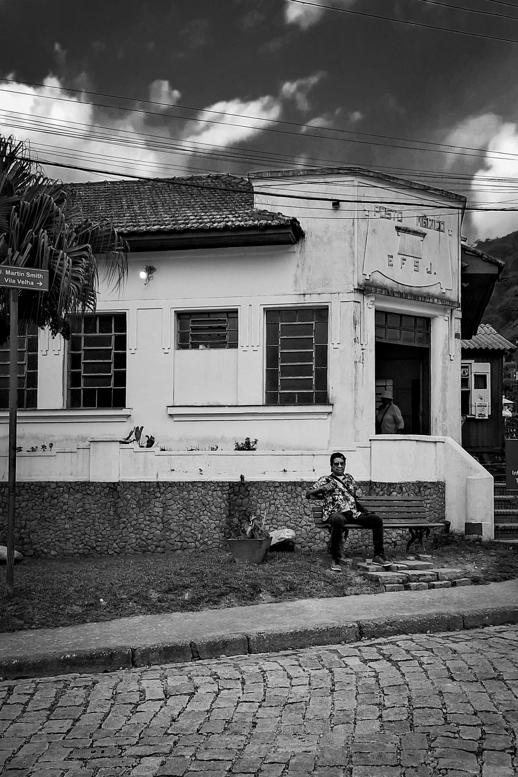 Black and white photo of an old building in Paranapiacaba, Brazil, with a person sitting outside.