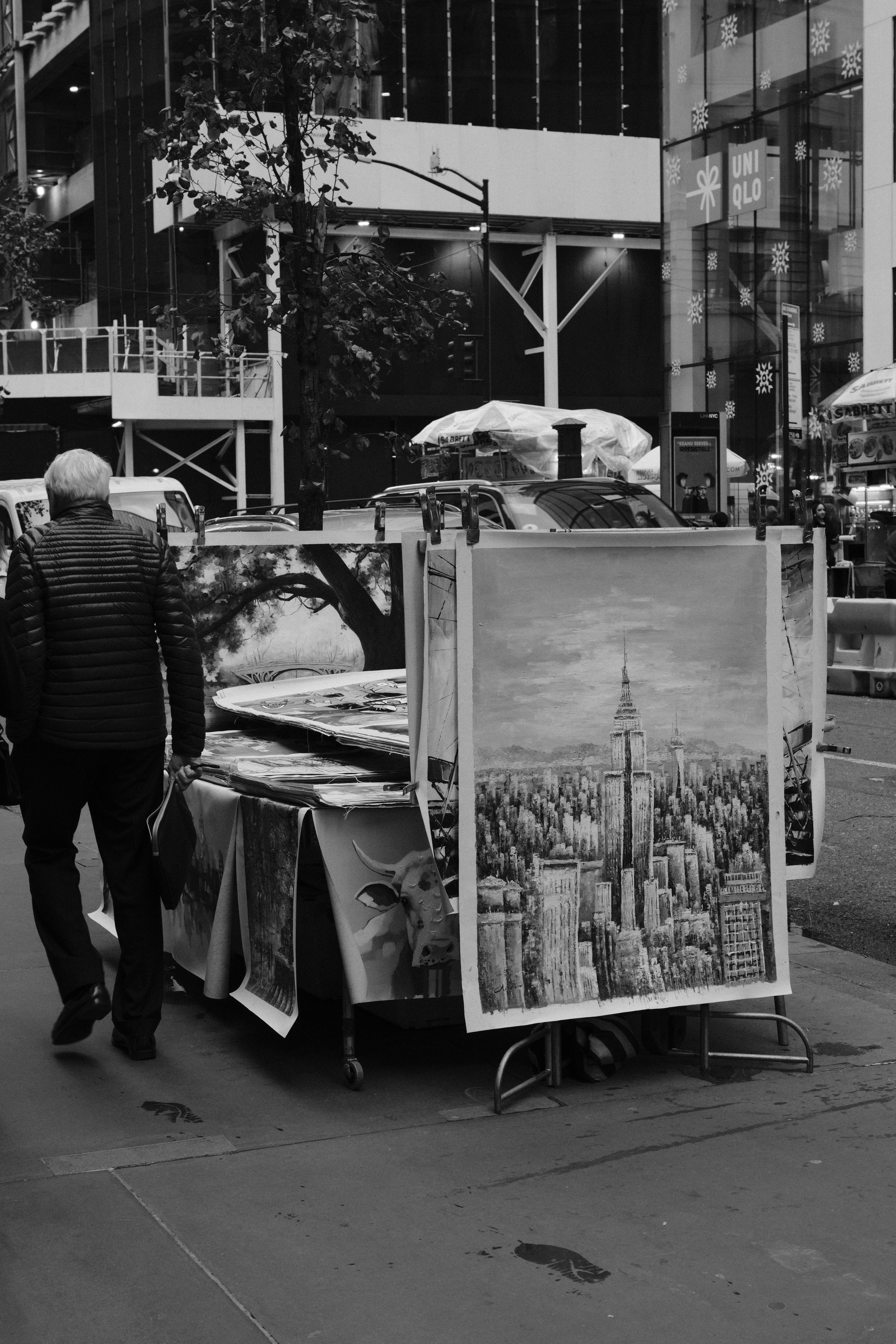 Black and white street scene with art display and pedestrian in New York City.