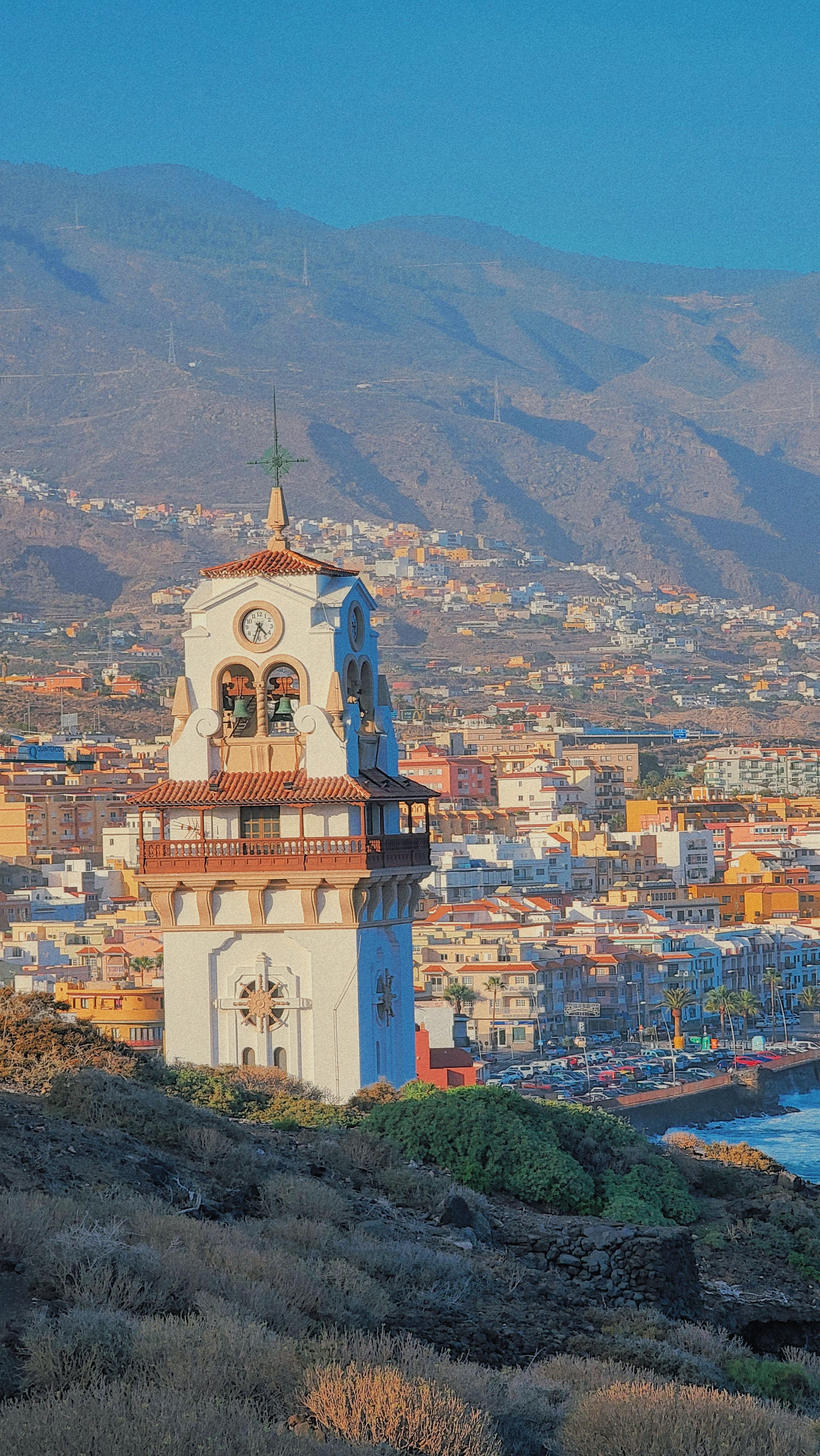 A picturesque view of a church tower in Candelaria, Spain with mountains in the background.