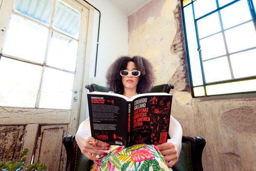 A woman with sunglasses reads a book in a brightly lit vintage interior, creating a serene atmosphere.