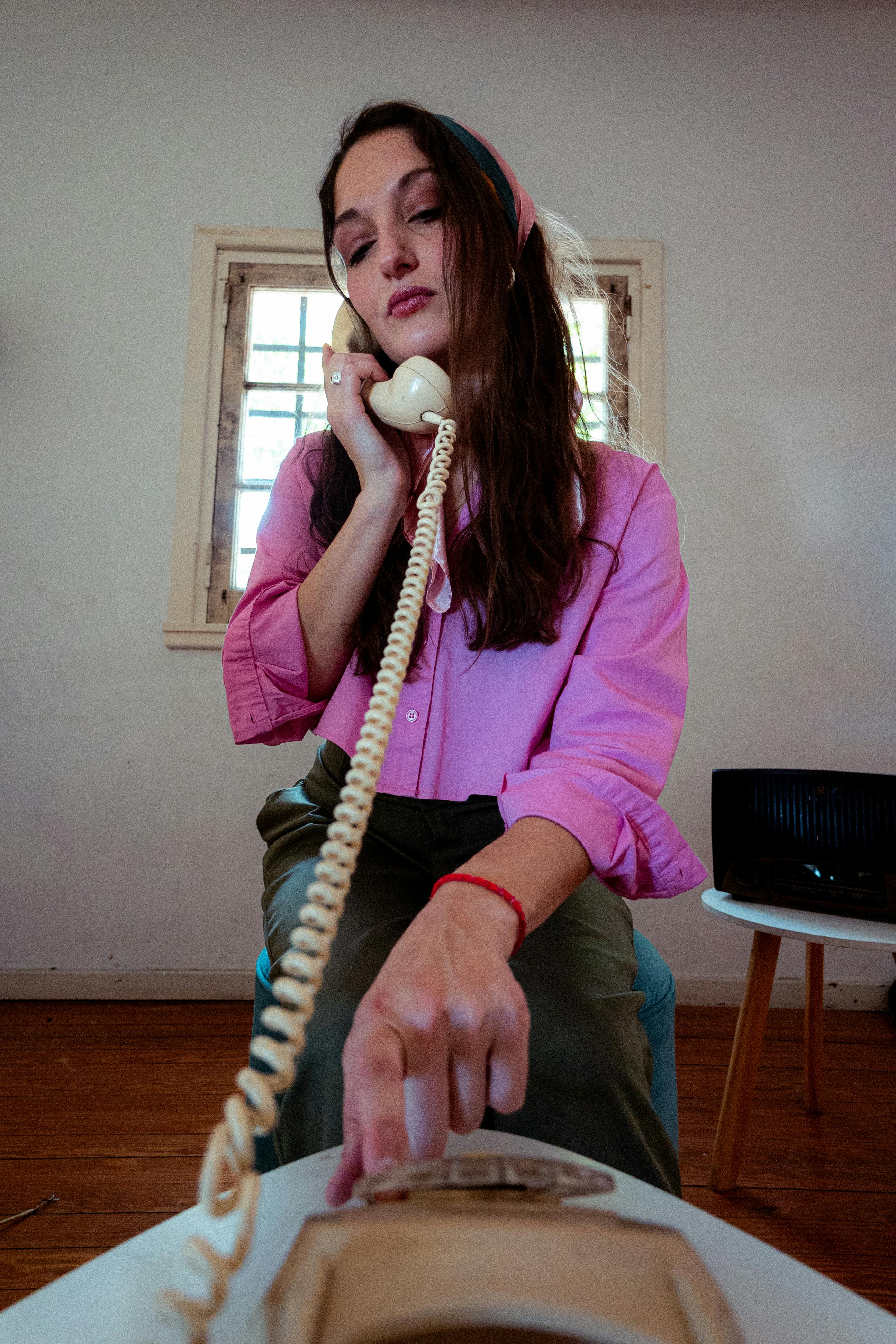 무료 아름다운 실내 환경에서 복고풍 핑크색 옷을 입은 여성이 빈티지 회전식 전화기를 사용하고 있습니다. 스톡 사진