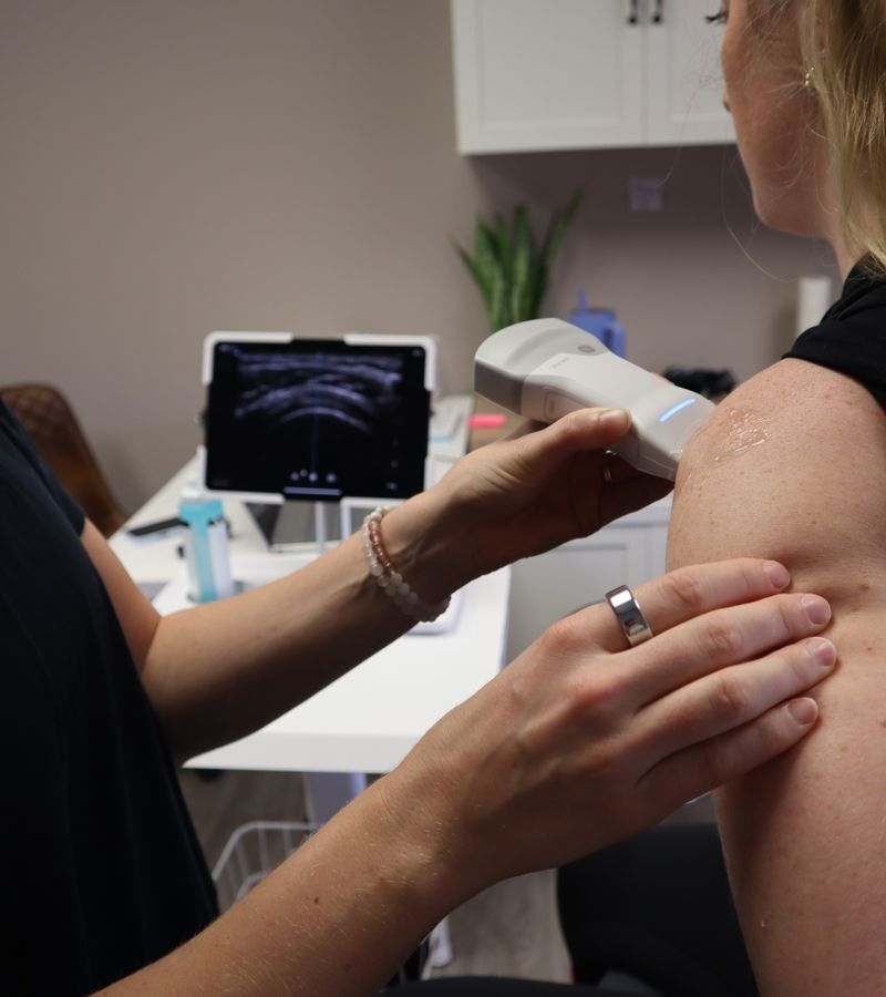 Ultrasound therapy being performed on a patient's shoulder by a medical professional in a clinic setting.