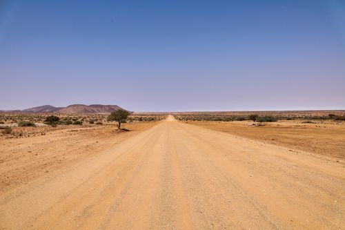 Free An expansive desert road stretches under a cloudless sky, leading towards distant mountains. Stock Photo