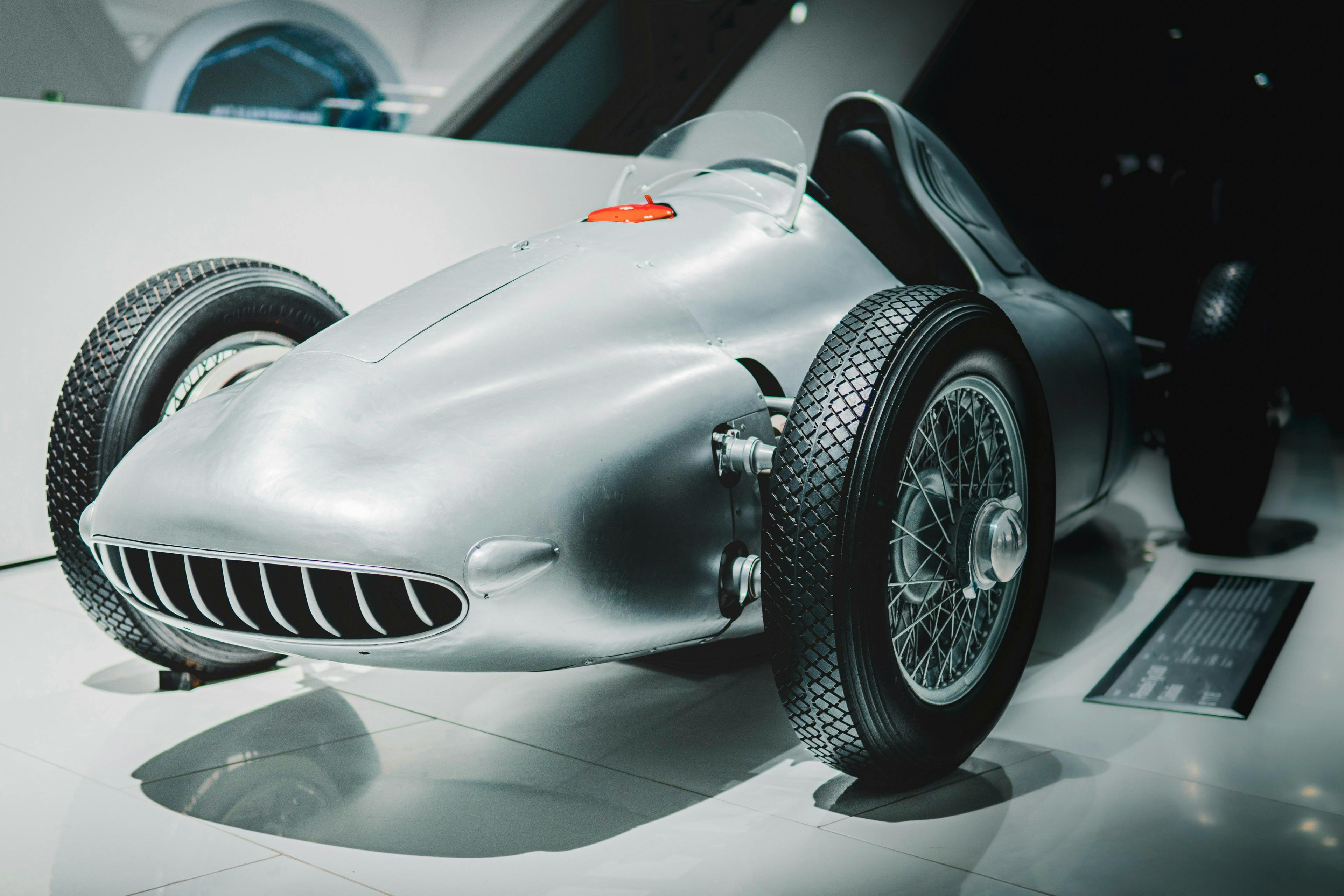 Free Vintage race car on display in a modern museum setting. Ideal for historical automotive concepts. Stock Photo