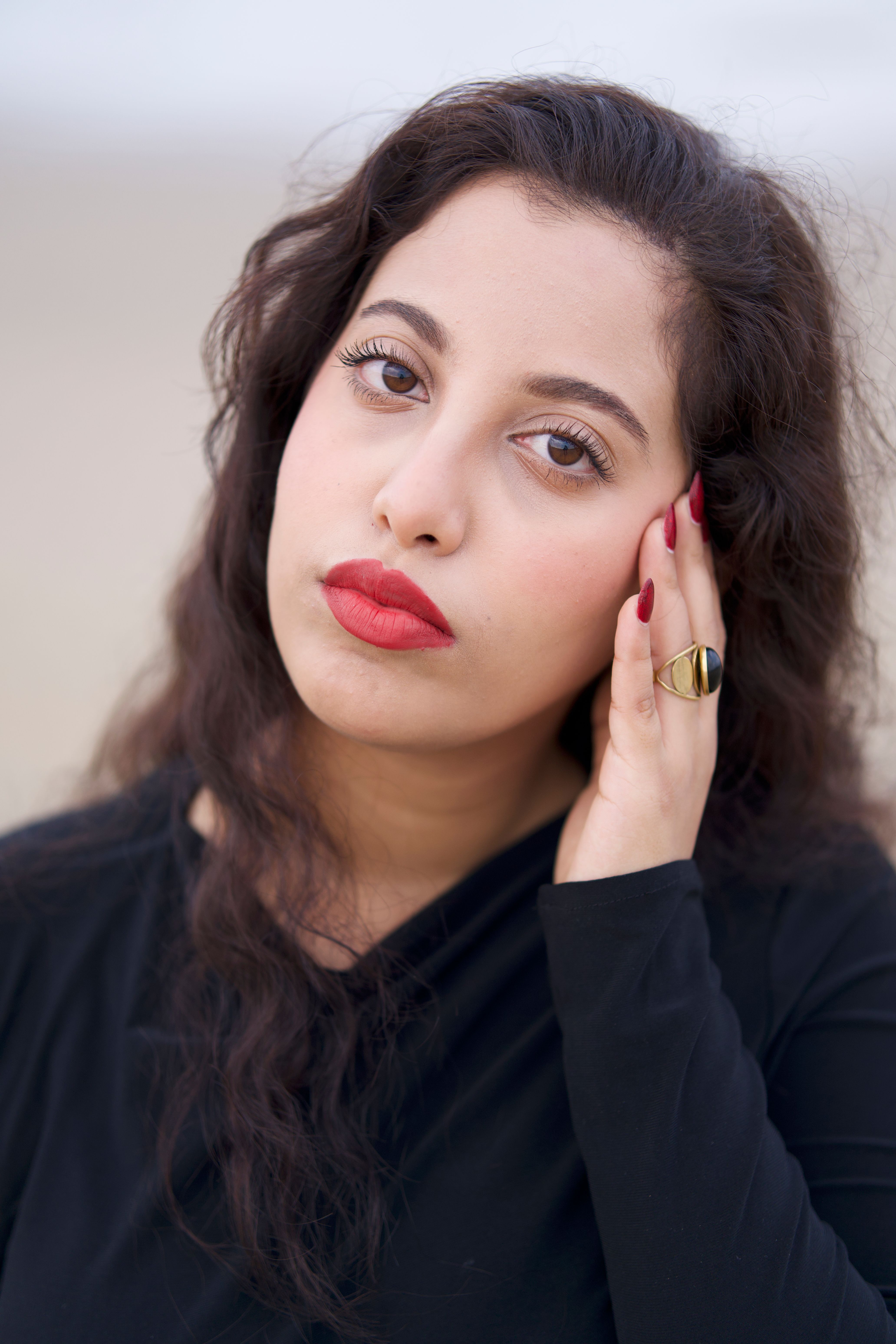 Elegant portrait of a woman with striking red lips and black outfit, expressing contemplation.