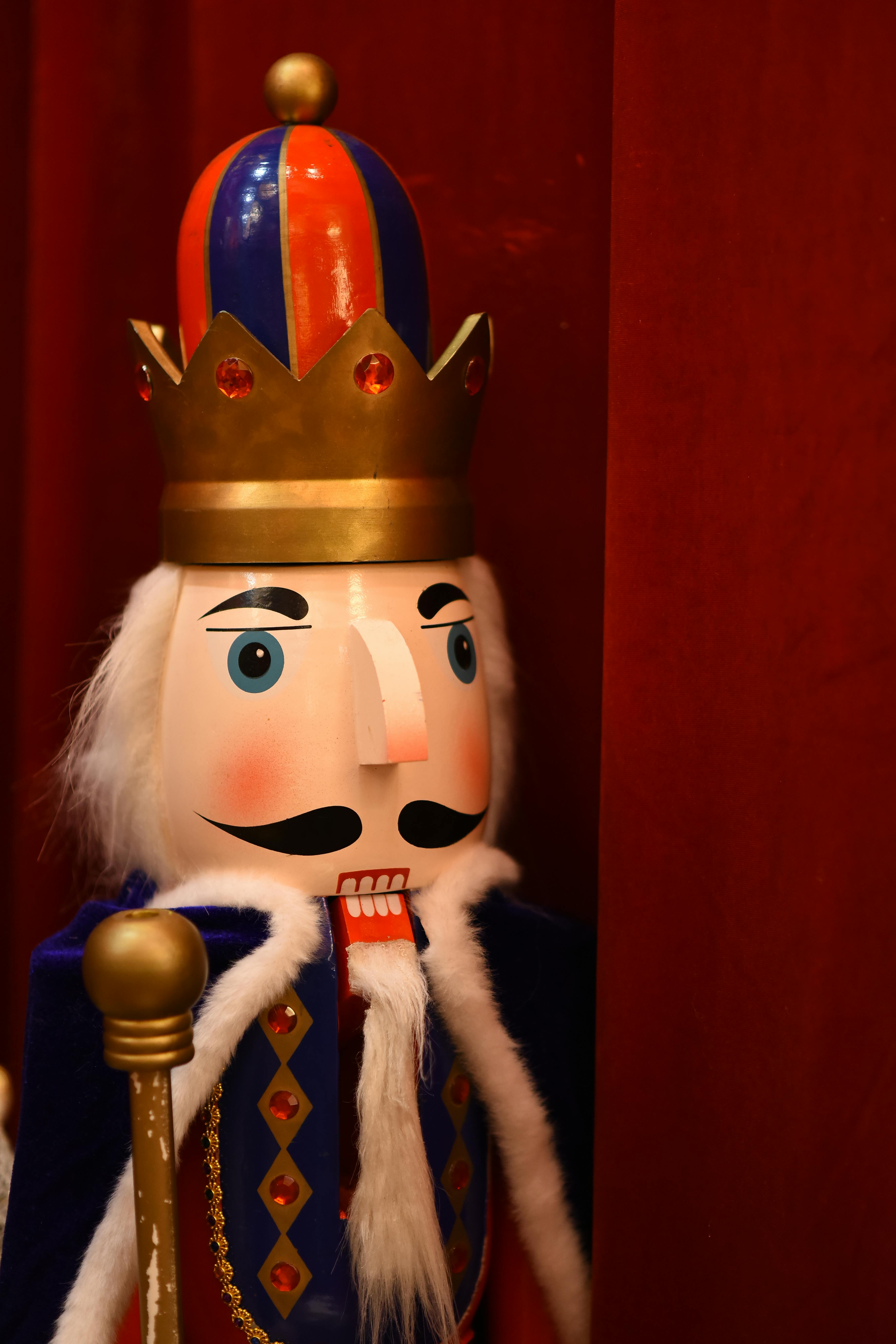 Ücretsiz Zengin kırmızı bir fon önünde, renkli bir taç takan ahşap fındıkkıran kral heykeli. Stok Fotoğraflar