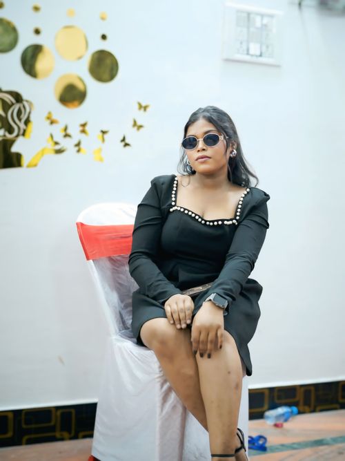 Free Stylish woman wearing black dress and sunglasses, seated indoors with decorative wall. Stock Photo