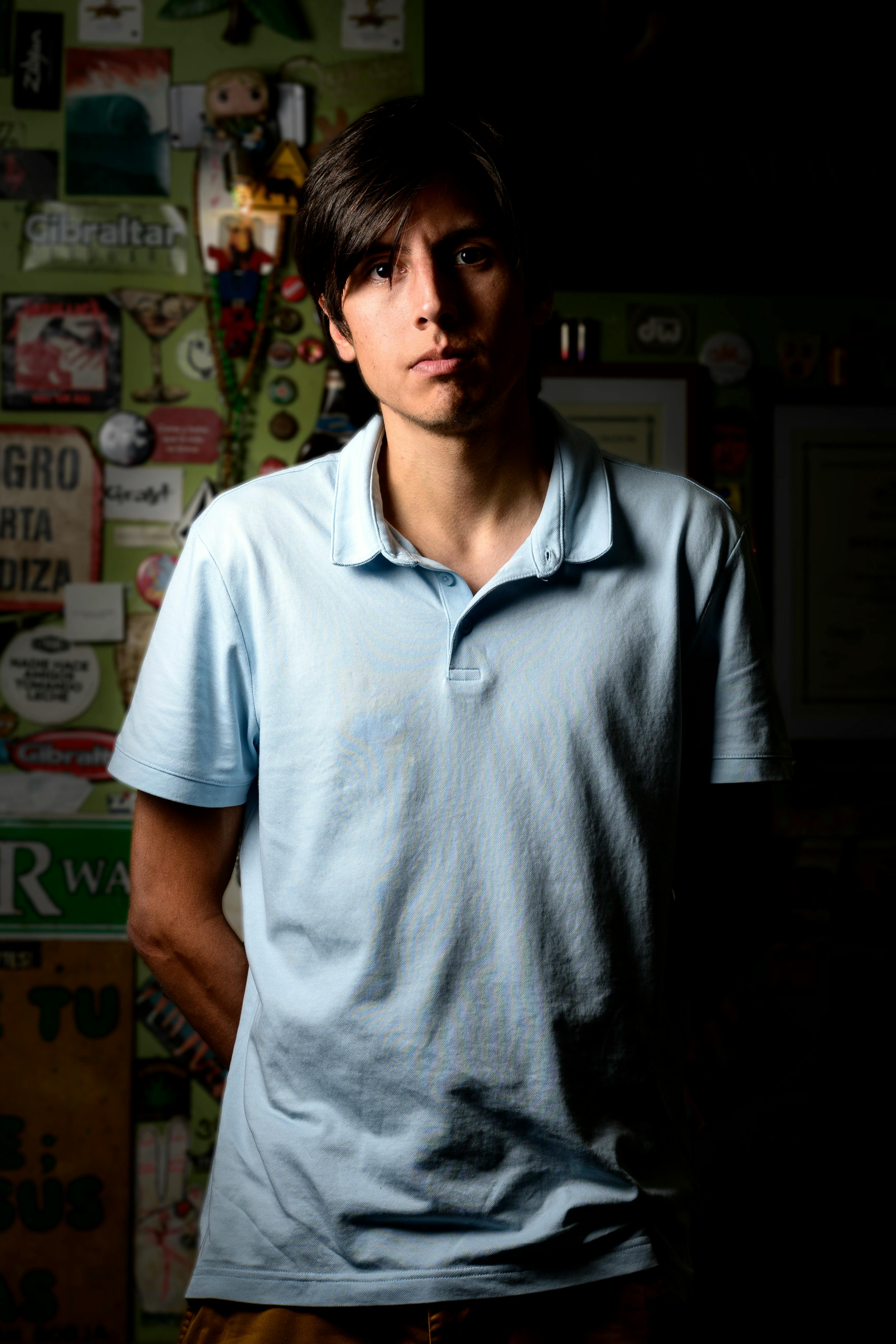 Portrait of a young man in a dimly lit room with mixed wall decor, creating a moody atmosphere.