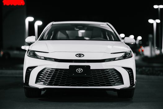 Close-up front view of a sleek white sedan car in a parking lot at night.