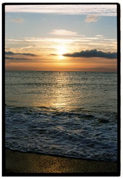 Peaceful beach sunset with waves and clouds, creating a serene ambiance.
