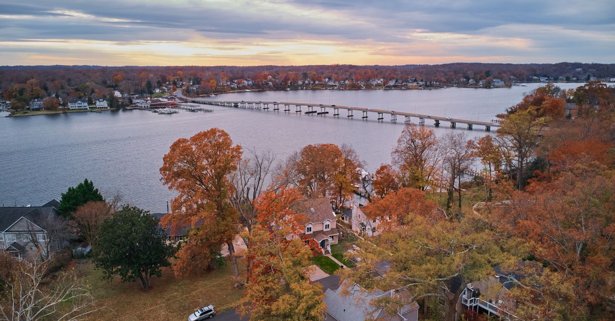 Stunning aerial view of lakeside homes with vibrant autumn foliage under a colorful sky.