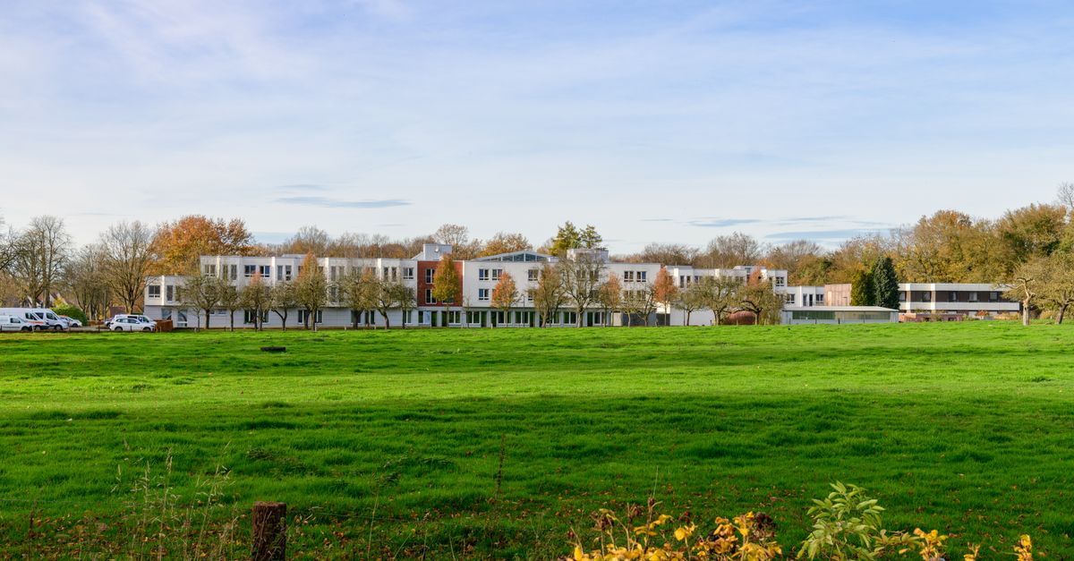Wide view of modern residential buildings surrounded by lush greenery and autumn foliage under clear sky.
