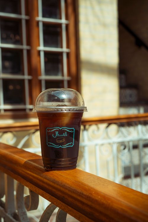 Free A refreshing iced coffee cup on a sunlit balcony railing, perfect for a summer day beverage. Stock Photo
