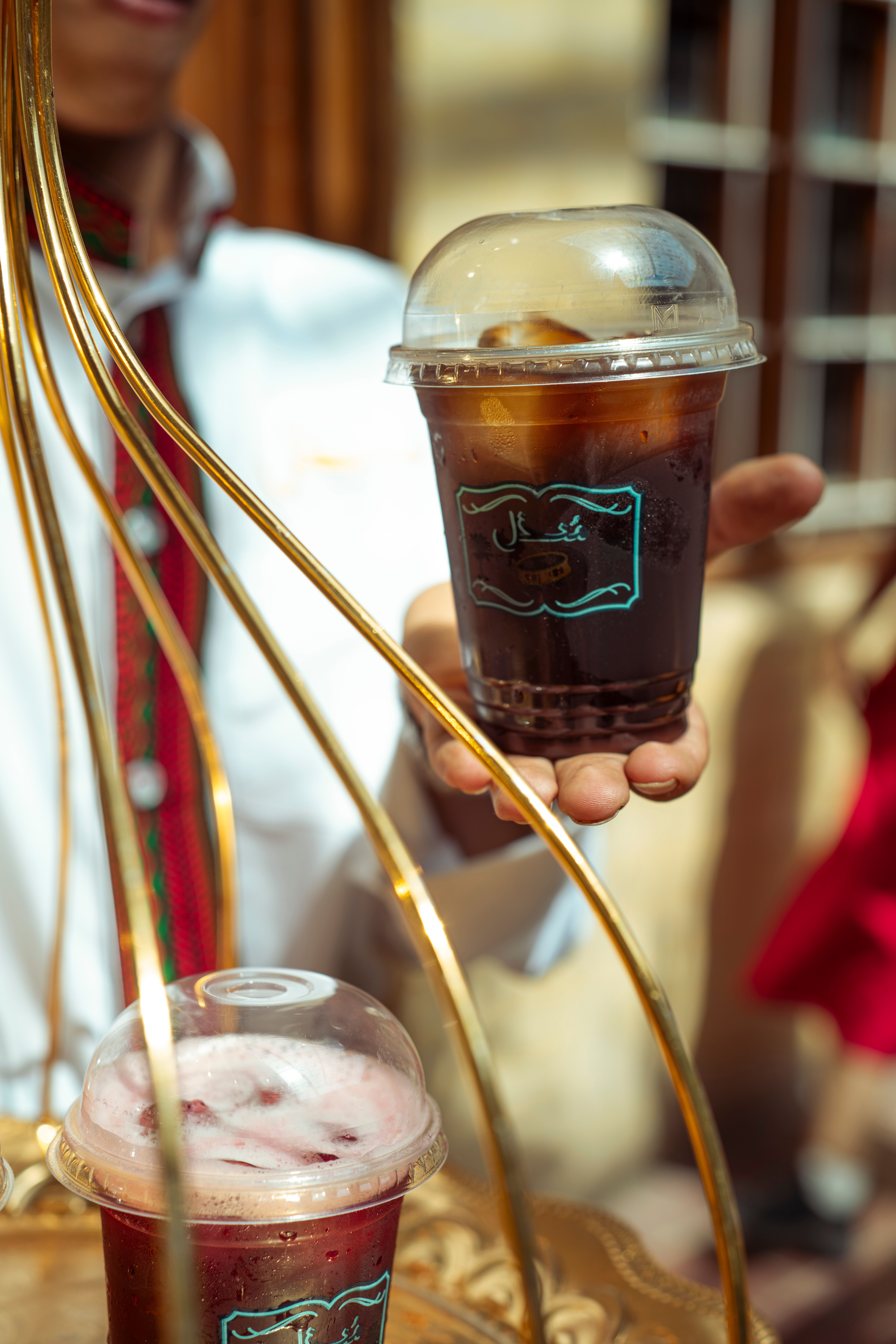 Close-up of a hand holding an iced coffee cup in an outdoor setting.