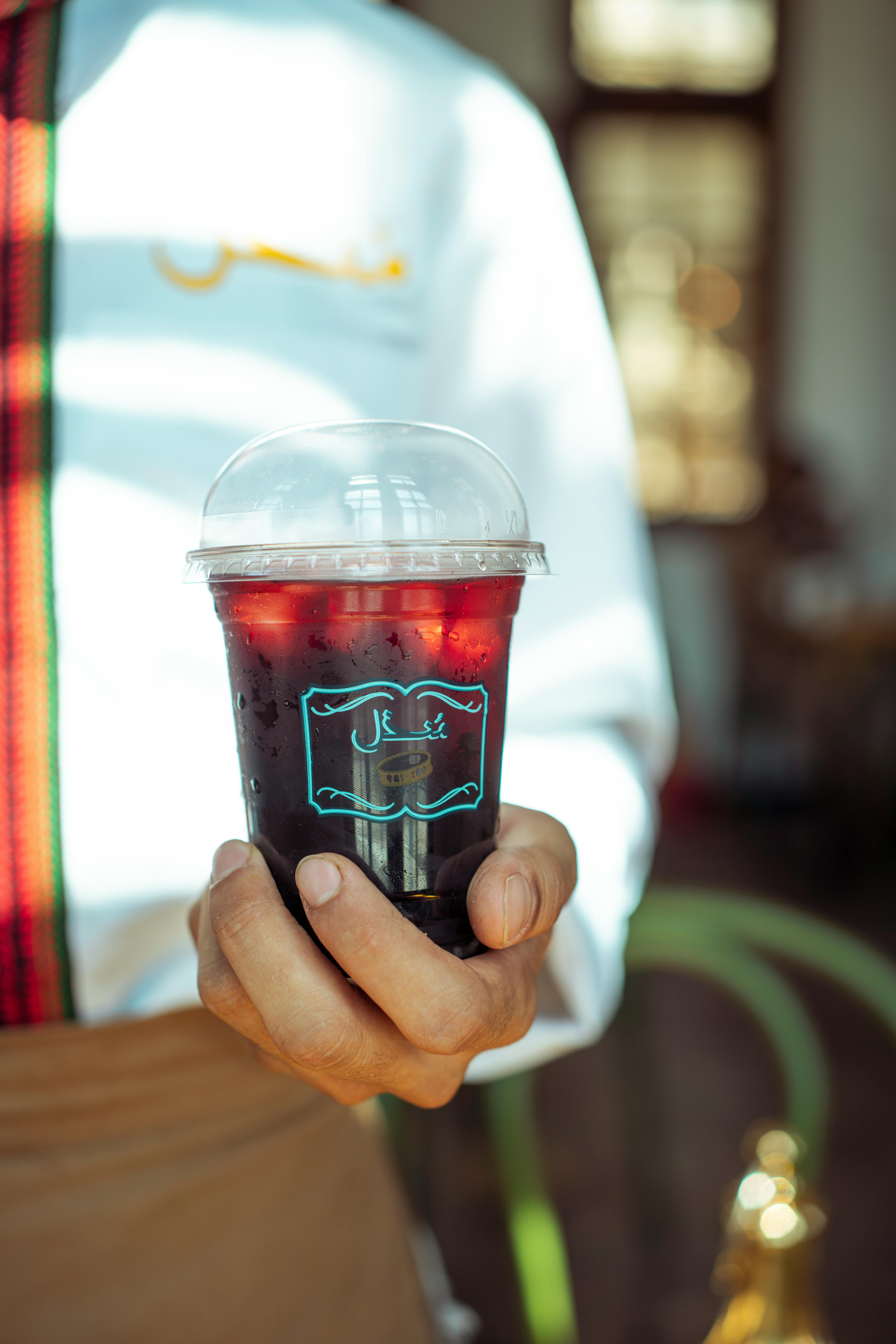 A barista presents a chilled, refreshing iced drink with Arabic text on the cup.