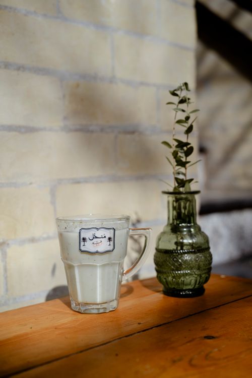 Free A glass of milk next to a decorative green vase on a wooden table casting shadows indoors. Stock Photo