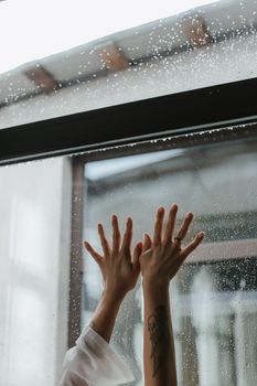 Close-up of hands touching a rainy window, conveying emotion and introspection.