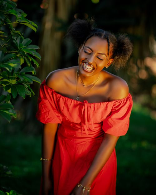 Free Joyful woman in a red dress smiling outside surrounded by greenery. Stock Photo