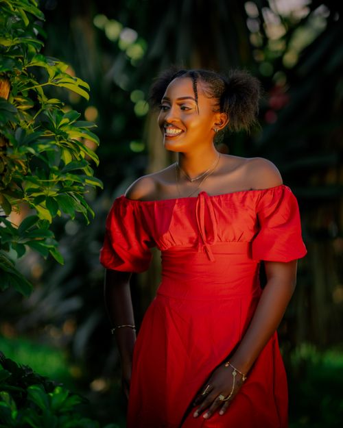 Free A woman in a red dress smiling among lush greenery outdoors. Stock Photo