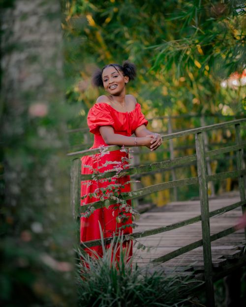 Free Smiling woman in a red dress, leaning on a wooden bridge outdoors. Stock Photo