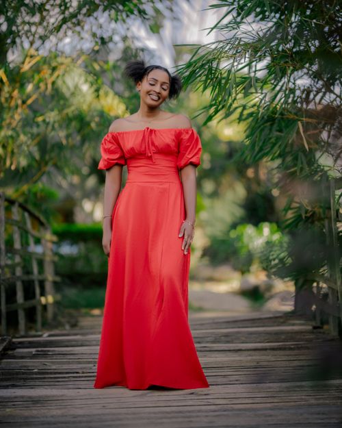 Free Woman in a stunning red gown stands on a wooden path surrounded by greenery. Stock Photo