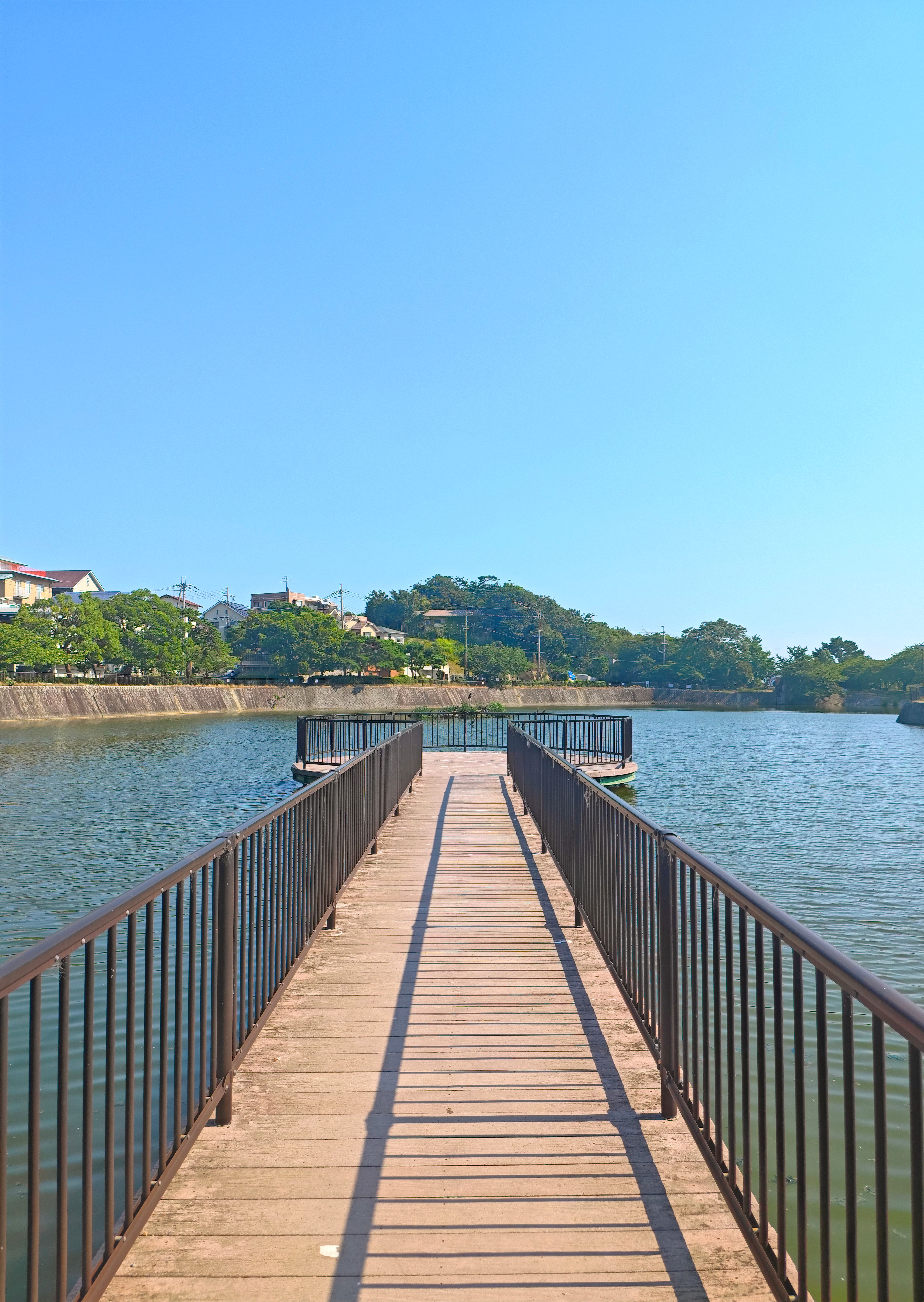 Experience the serene beauty of Nishinomiya city with a calm river view from a wooden pier under a clear blue sky.