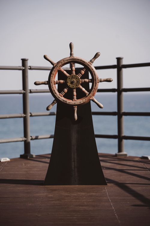 Free Rustic ship wheel on a wooden waterfront deck with ocean views. Stock Photo