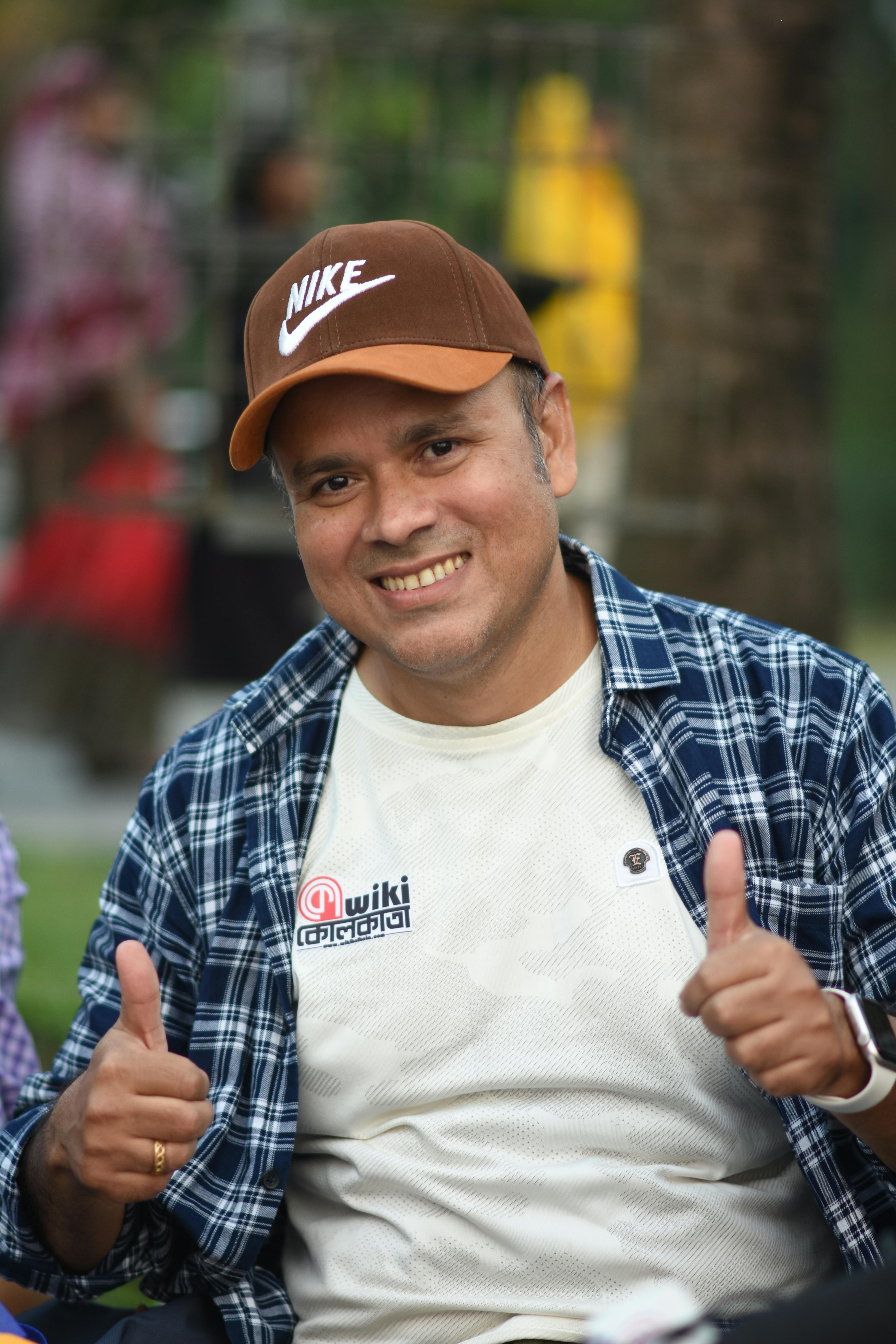 Cheerful man in casual attire giving a thumbs up in a Kolkata park setting.