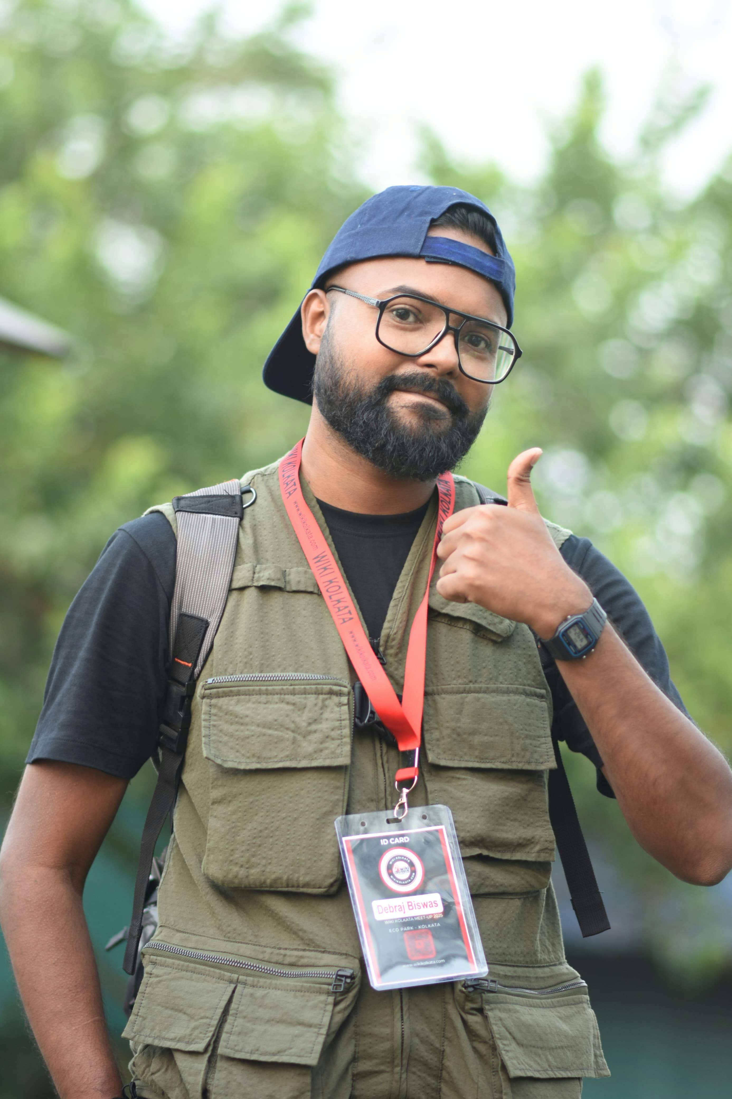 A cheerful man with glasses gives a thumbs up while standing outdoors in Kolkata, India.