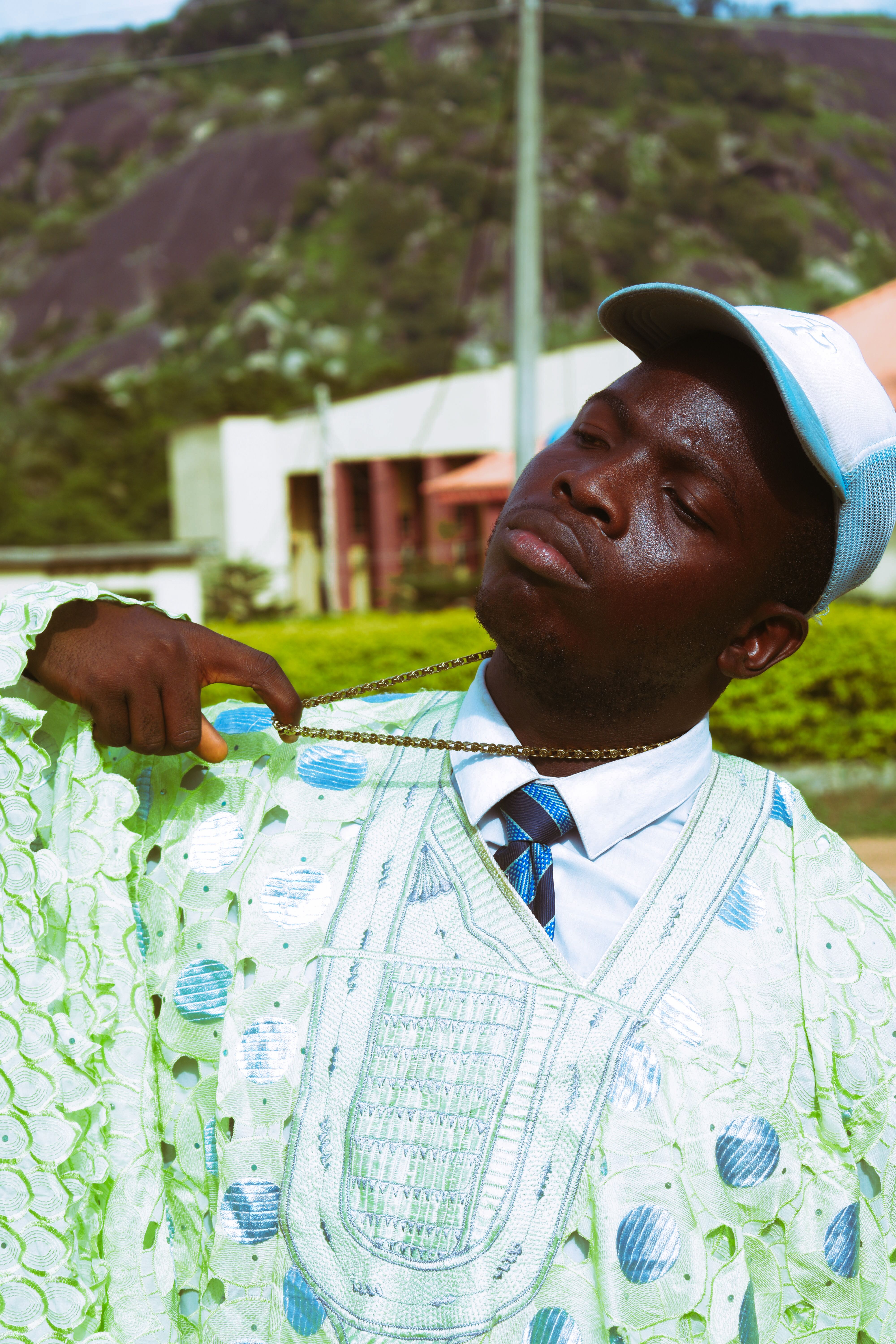 Young African man in traditional attire proudly displaying a chain outdoors on a sunny day.
