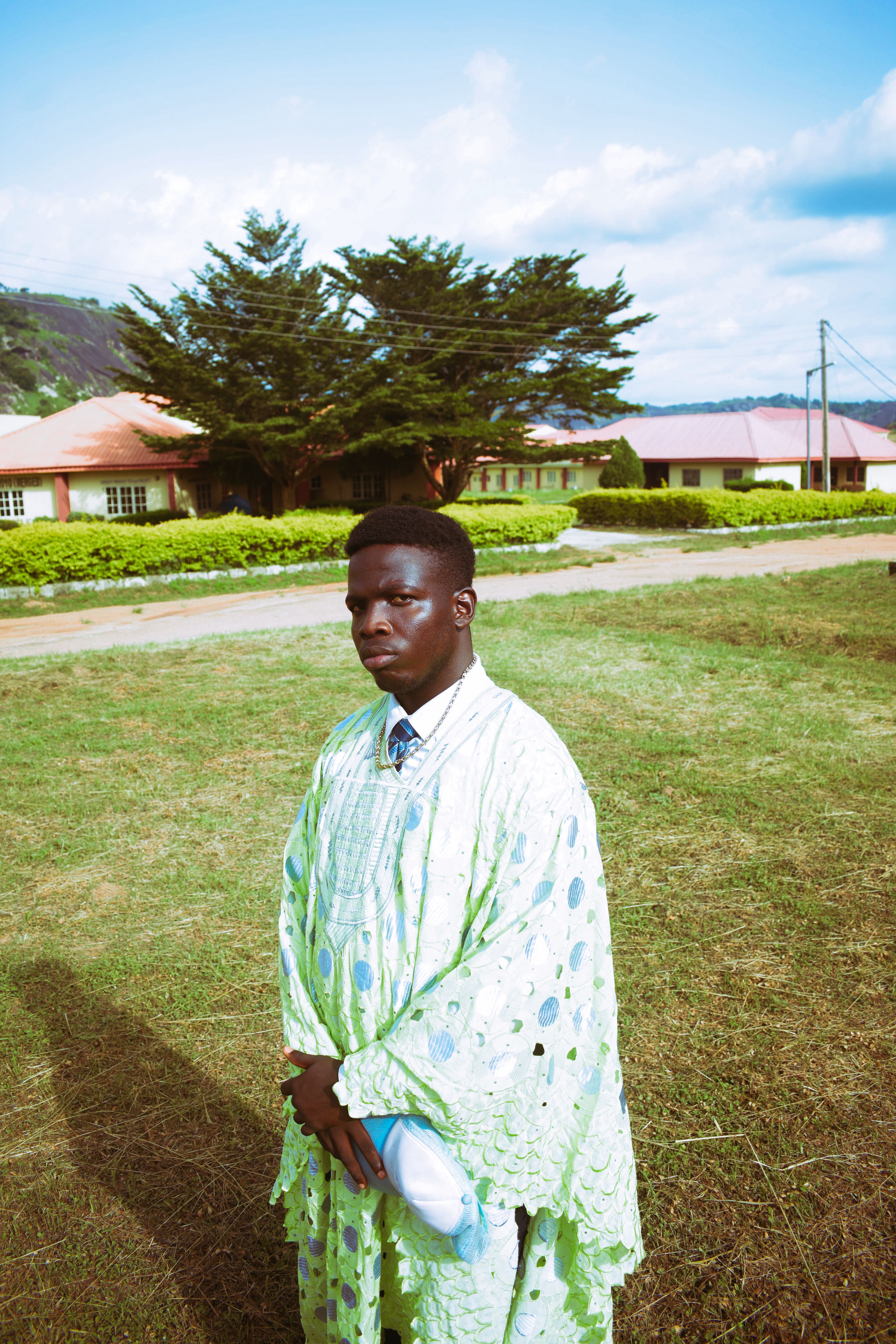 Portrait of a young man in traditional Nigerian attire standing outdoors in a serene setting.