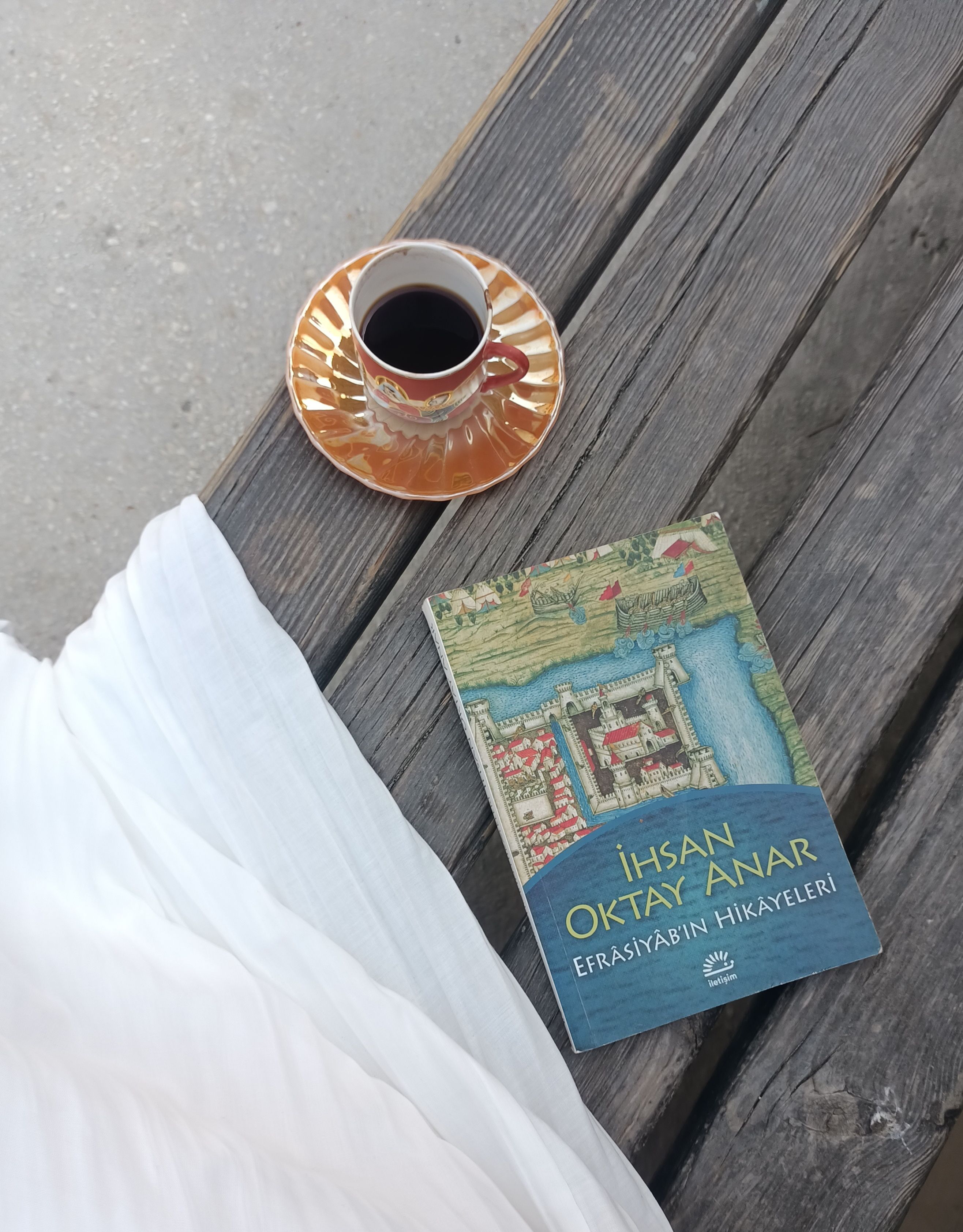 A cozy scene with Turkish coffee and a book on a wooden bench outdoors.