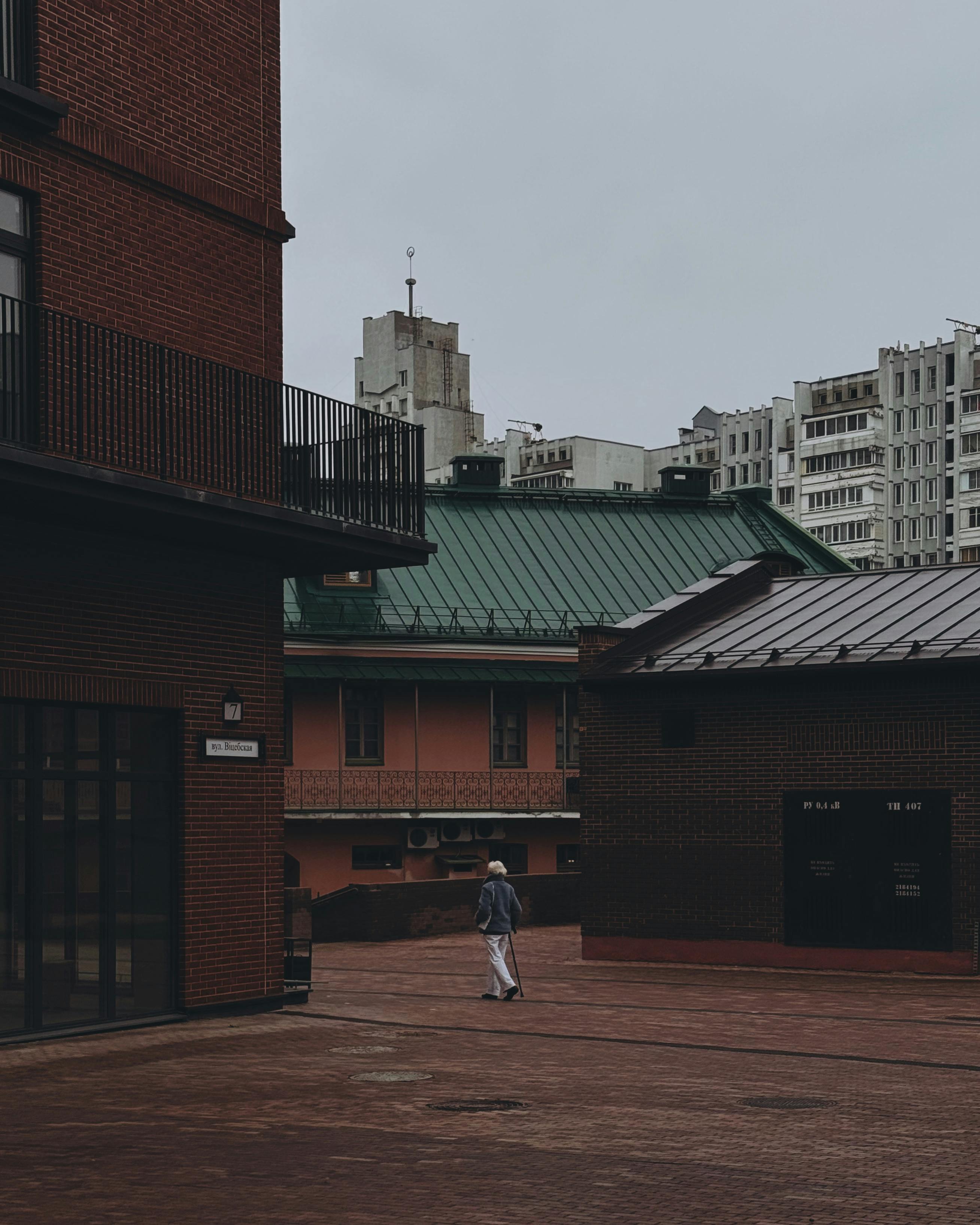 Gratis En person går gjennom en mursteinsgate omgitt av moderne bygninger under en overskyet himmel. Arkivbilde