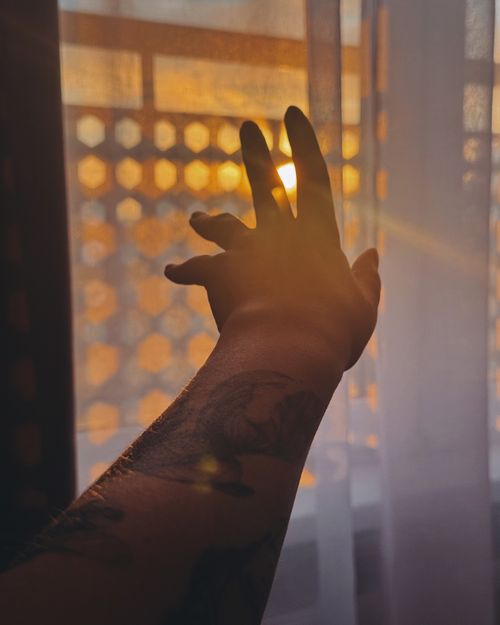 Free An arm with tattoos reaches toward sunlight filtering through a curtain. Stock Photo