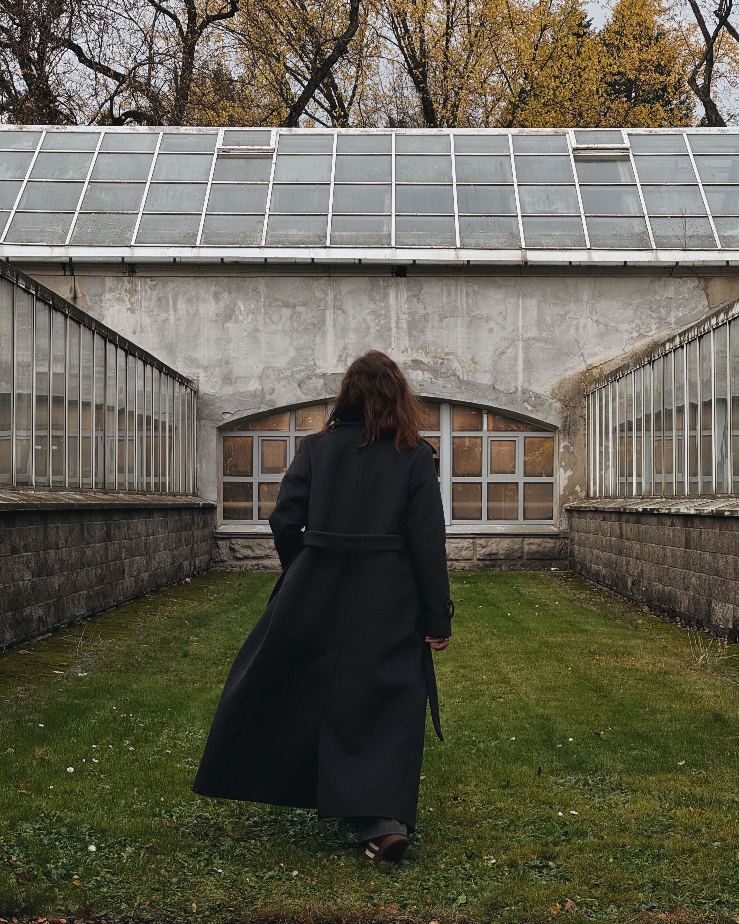 Woman in Black Coat Walking Towards Greenhouse · Free Stock Photo