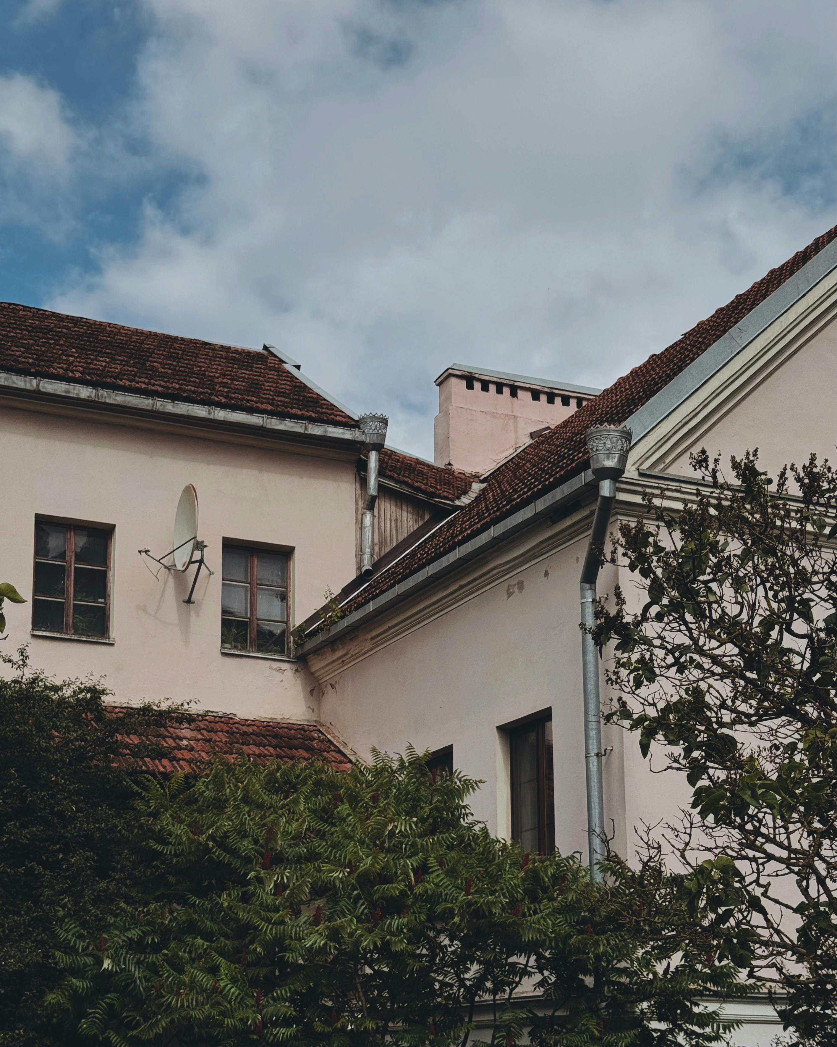 A vintage building with a red tiled roof under a clear blue sky, surrounded by greenery.