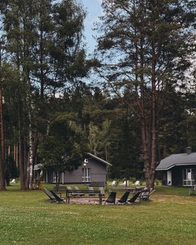 Charming woodland cottages surrounded by tall trees and a cozy fire pit area, perfect for summer relaxation.