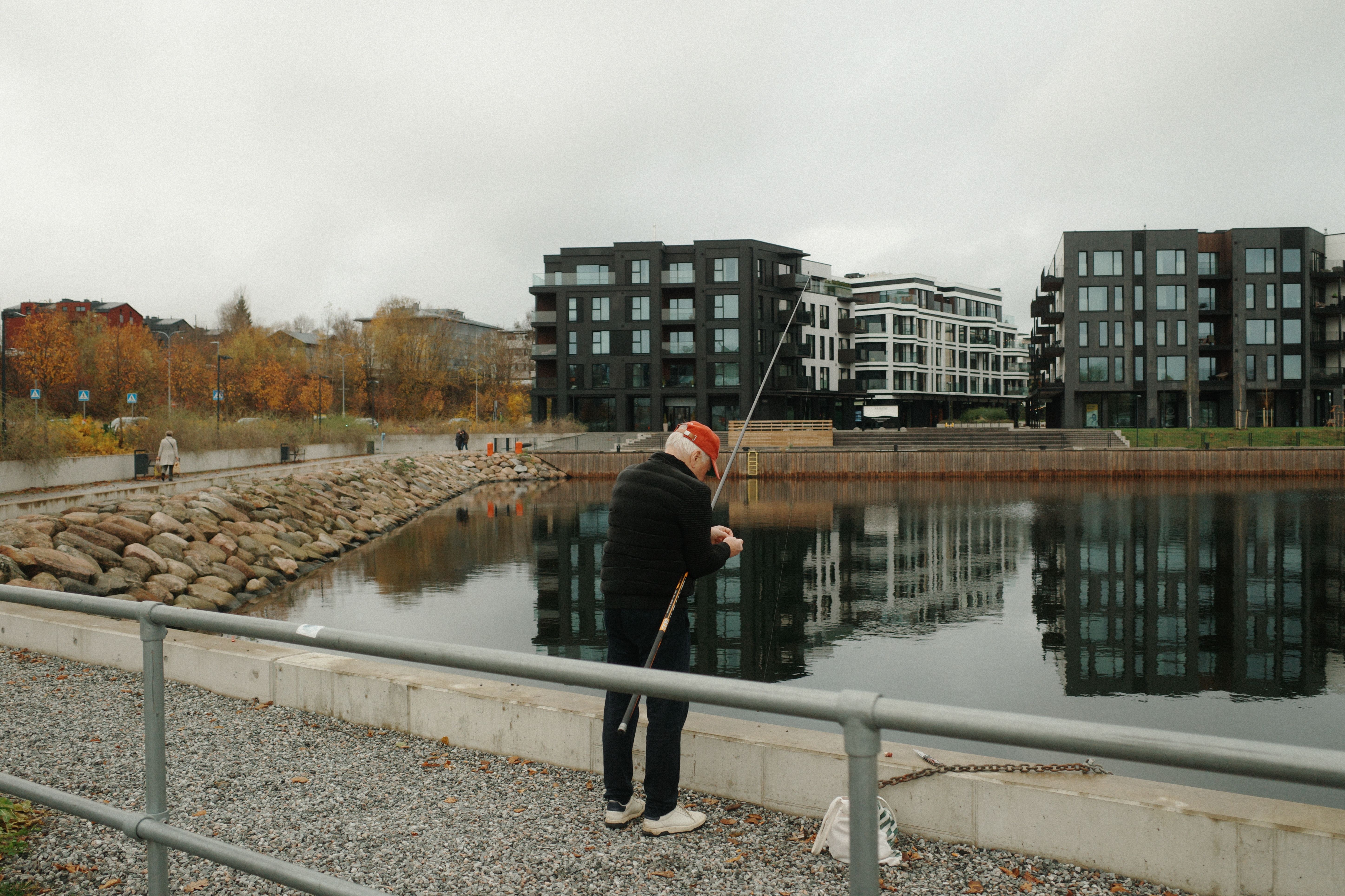 Elderly Man Fishing by Modern Waterfront · Free Stock Photo