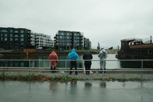 Four people in rain gear at a waterfront, surrounded by modern buildings.