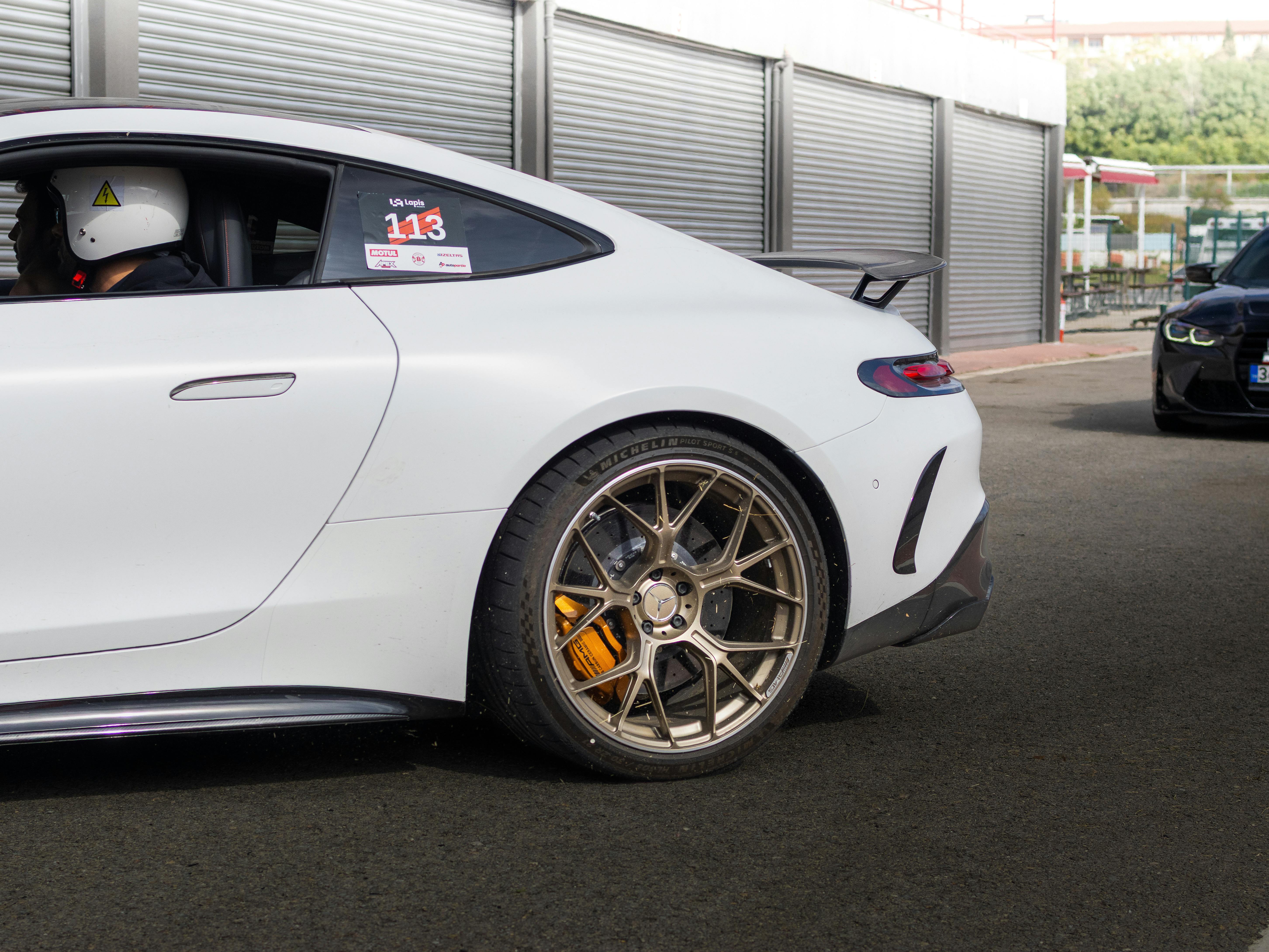 Close-up of a white sports car with helmeted driver on a race track.